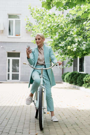 senior business lady using mobile phone while sitting on bicycle outdoorsの写真素材