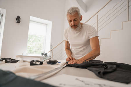 Mature designer measuring cloth on tableの写真素材