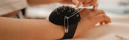 Cropped view of designer with pincushion and needles, banner