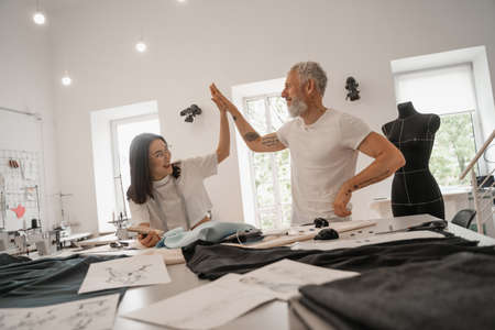 Smiling interracial designers giving high five near cloth in studioの写真素材