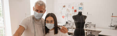 Multiethnic designers in protective masks standing in atelier, banner