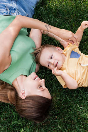 top view of cheerful mother spending time with happy toddler son while lying on grassの写真素材