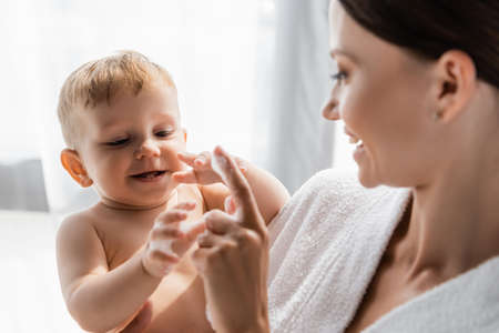 happy toddler boy touching bath foam near happy mother in bathrobeの写真素材