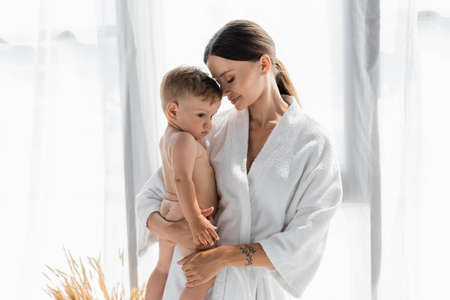 caring mother in bathrobe holding in arms naked toddler sonの写真素材