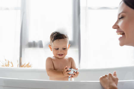 happy toddler boy holding shower head near blurred and cheerful mother on foregroundの写真素材