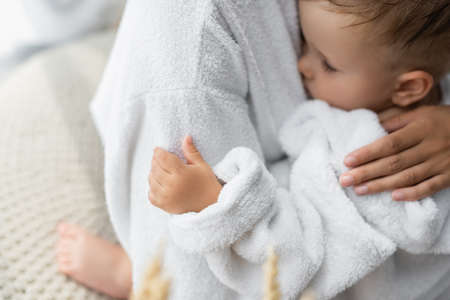 mother hugging toddler son with closed eyes in bathrobeの写真素材