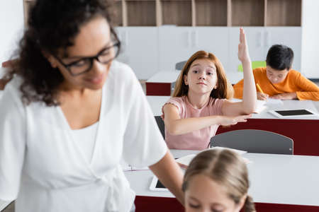 redhead girl raising hand near blurred african american teacher during lessonの写真素材