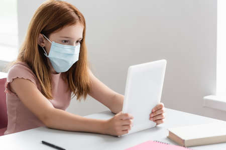 girl in medical mask looking at digital tablet during school lessonの写真素材
