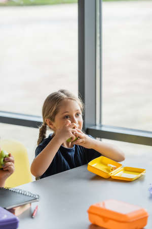 schoolgirl eating fresh apple in school dining roomの写真素材