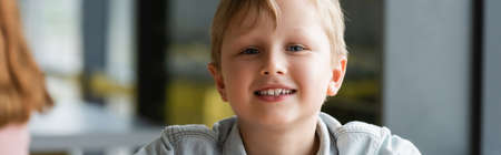 joyful schoolboy smiling at camera during lesson, banner