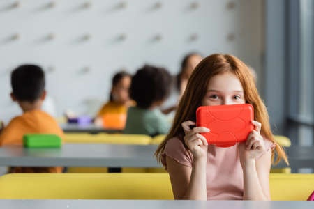 redhead schoolgirl obscure face with lunch box in eatery