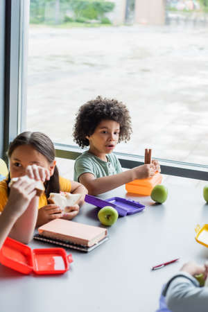 interracial kids eating sandwiches in school canteenの写真素材