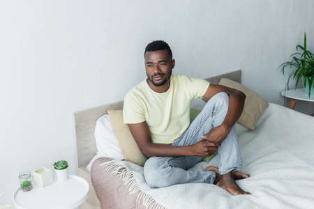 barefoot african american man looking away while sitting on bed