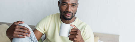 african american man holding mug with coffee, bannerの写真素材