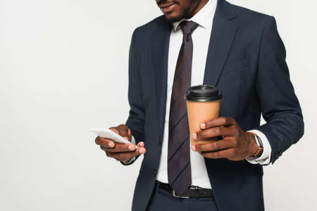 cropped view of african american businessman in suit messaging on smartphone and holding paper cup...
