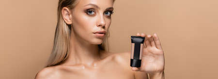 young blonde woman showing tube with face foundation isolated on beige, bannerの写真素材