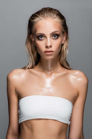 wet woman in white top with bare shoulders posing isolated on grayの写真素材
