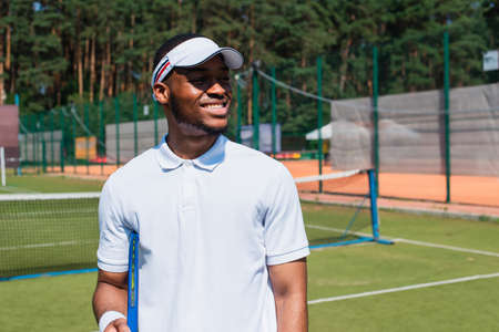 Smiling african american tennis player holding racket on courtの写真素材