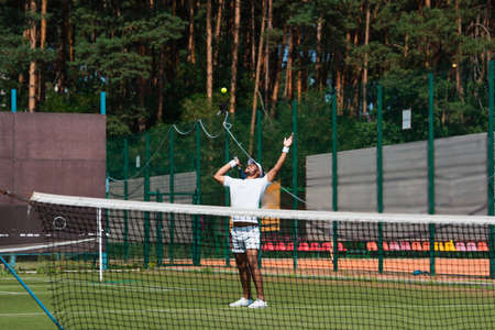 Excited african american sportsman looking at ball near net on tennis court