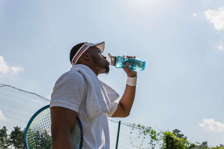Low angle view of african american tennis player drinking water on courtの写真素材