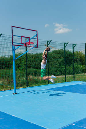 Young sportsman with basketball ball jumping under hoop on playground
