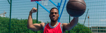 African american basketball player holding ball and showing muscles on playground, bannerの写真素材
