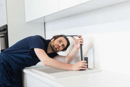 plumber checking faucet in contemporary kitchen
