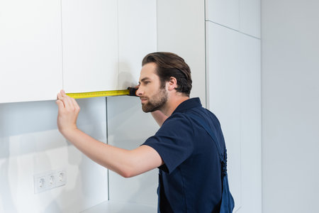 handyman measuring white furniture in modern kitchenの写真素材