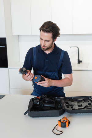 repairman holding electric drill near case in kitchenの写真素材
