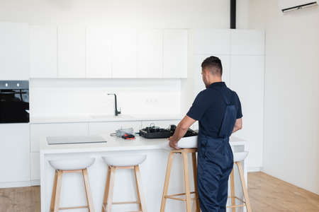 repairman in overalls holding stool near table with tools in kitchenの写真素材