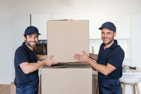 movers smiling at camera while stacking carton packages in kitchen