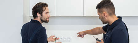 workman pointing at power sockets near electrician in kitchen, bannerの写真素材