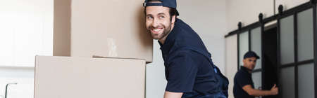 happy mover smiling near cardboard packages and blurred colleague, bannerの写真素材