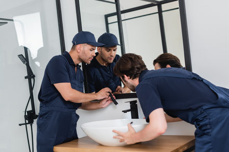 plumbers checking sink in bathroom with flashlight
