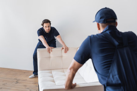 workmen moving white sofa together with colleague on blurred foregroundの写真素材