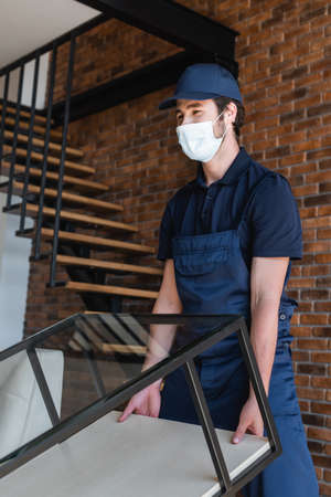 mover in medical mask lifting glass table near stairsの写真素材