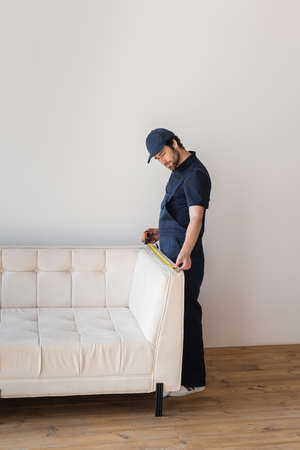 workman in uniform measuring white couch in living roomの写真素材