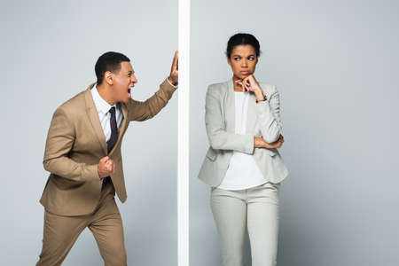 angry african american businessman screaming near wall and pensive businesswoman on grayの写真素材