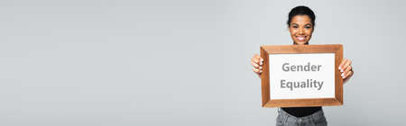 happy african american woman holding placard with gender equality lettering isolated on gray, bannerの写真素材