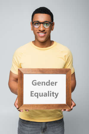 happy african american man holding placard with gender equality lettering isolated on grayの写真素材