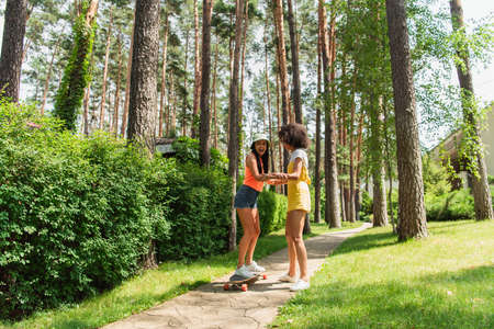 Excited interracial lesbian couple riding skateboard in parkの写真素材