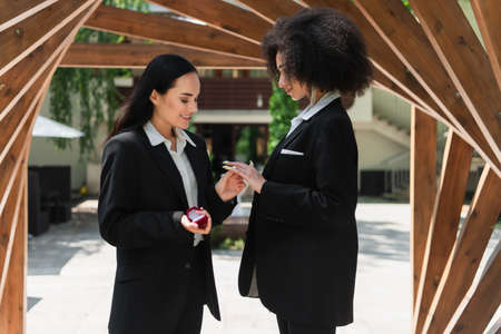 Smiling woman wearing wedding ring on finger of african american girlfriend in parkの写真素材