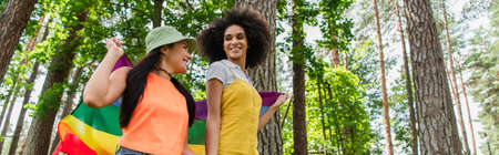 Low angle view of smiling african american woman holding lgbt flag with girlfriend outdoors, bannerの写真素材
