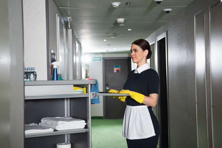 young maid holding handle of housekeeping cartの写真素材