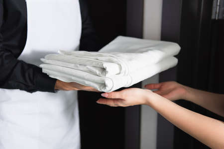 cropped view of maid housekeeper giving clean bed sheets to maidの写真素材