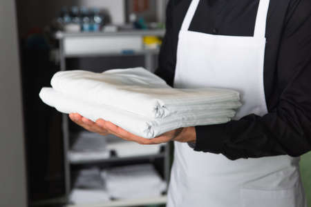 cropped view of housekeeper holding white clean bed sheetsの写真素材
