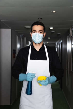 housekeeper in medical mask and rubber gloves holding spray bottle with ragの写真素材
