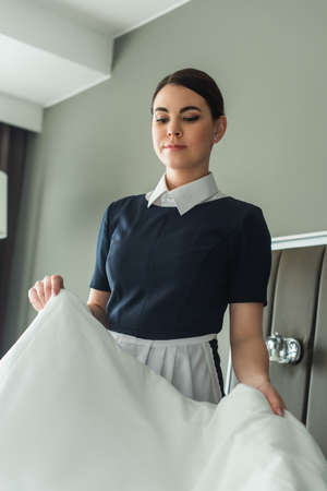 young chambermaid changing white bedding in hotel room