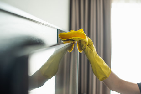 partial view of housekeeper in rubber glove cleaning tv display with rag