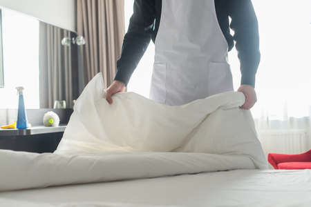 cropped view of housekeeper changing white bedding in hotel roomの写真素材